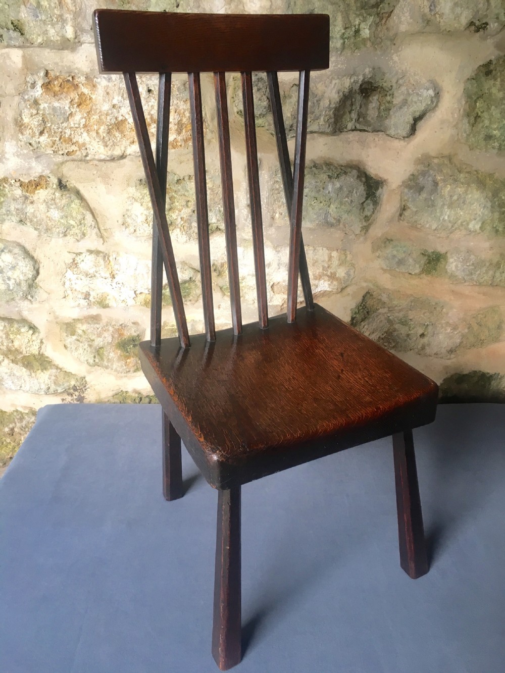 A dark oak side chair featuring a spindle back rest, solid wooden seat, and tapered splayed legs. View X