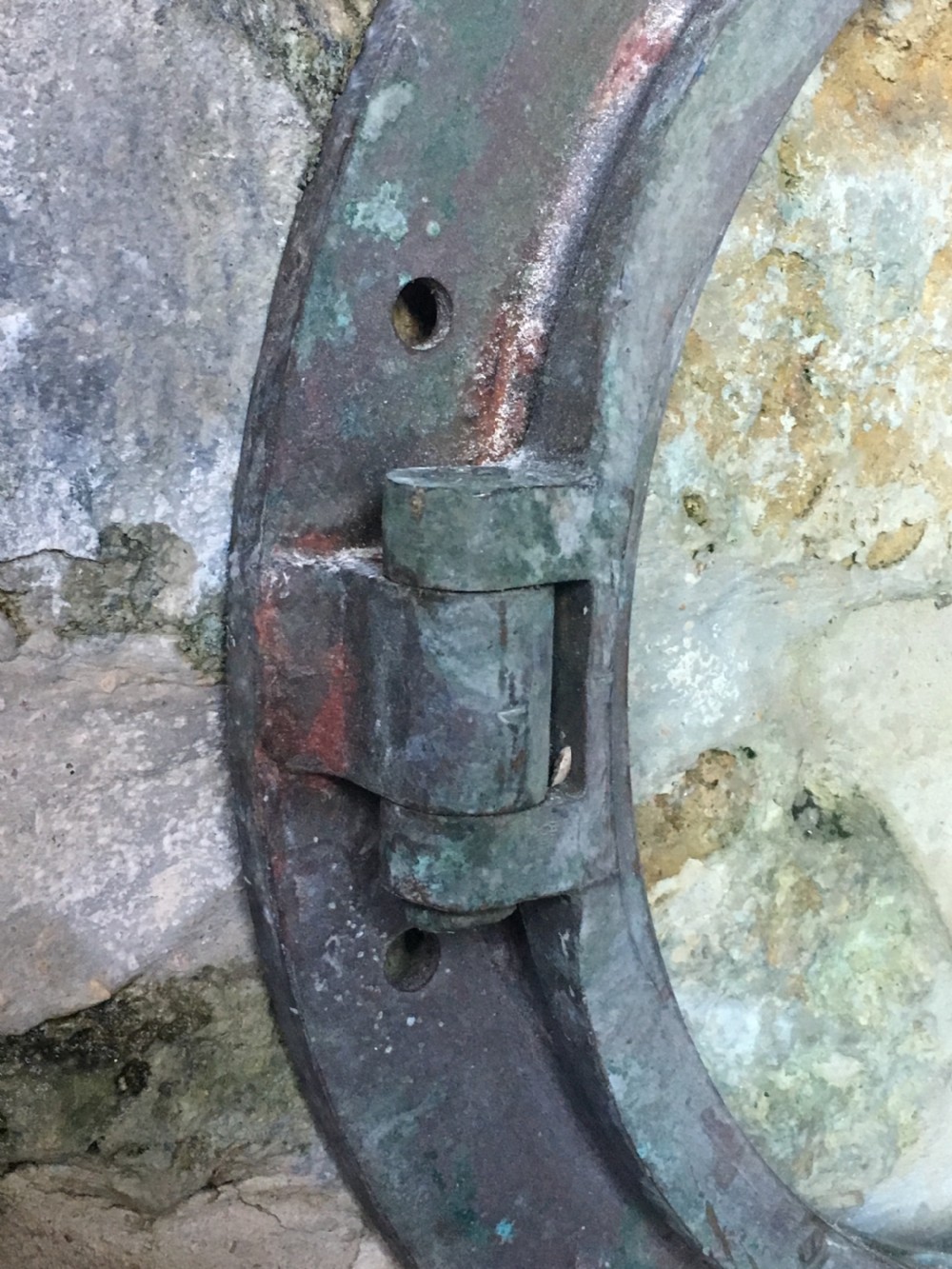 A heavy antique bronze circular ship porthole featuring visible hinge mounts, dog-bolt fasteners, a clear glass pane, and natural green patina. View IV