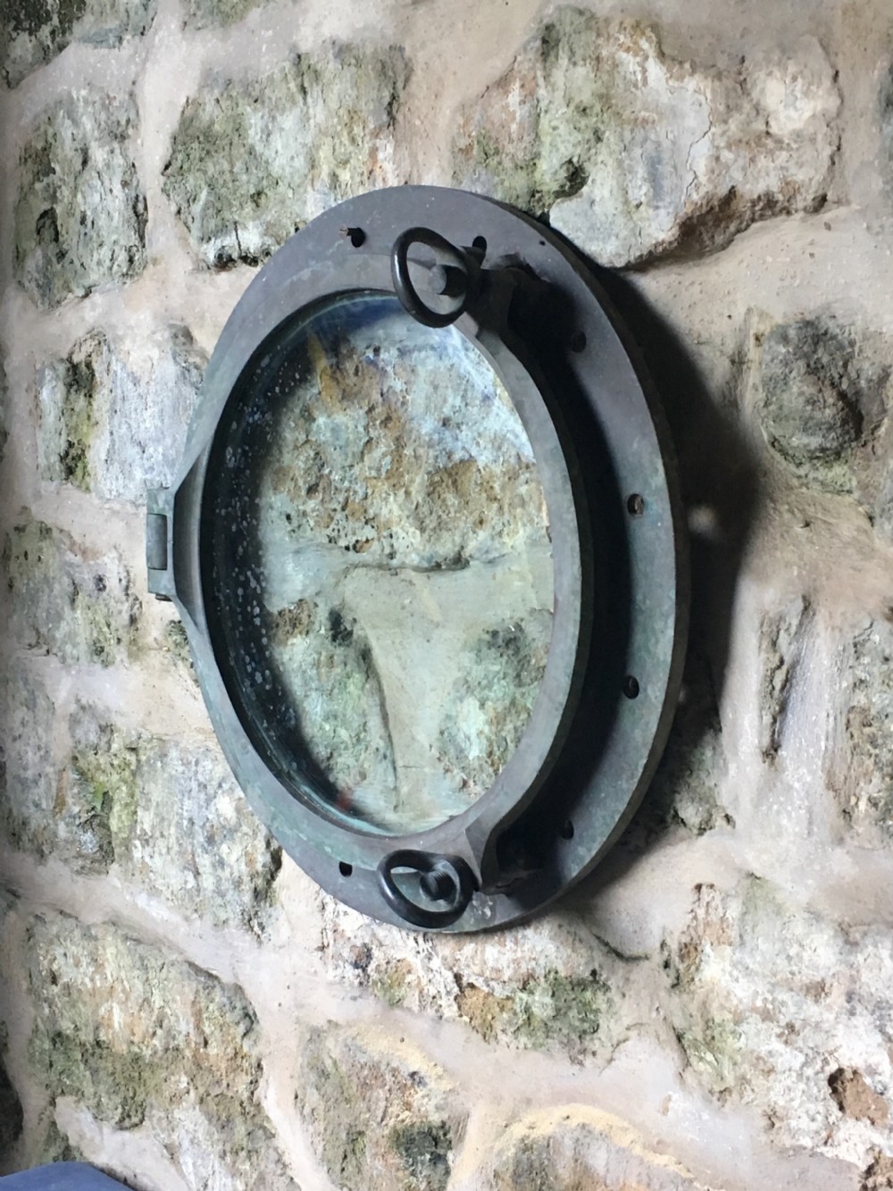 A heavy antique bronze circular ship porthole featuring visible hinge mounts, dog-bolt fasteners, a clear glass pane, and natural green patina. View VIII