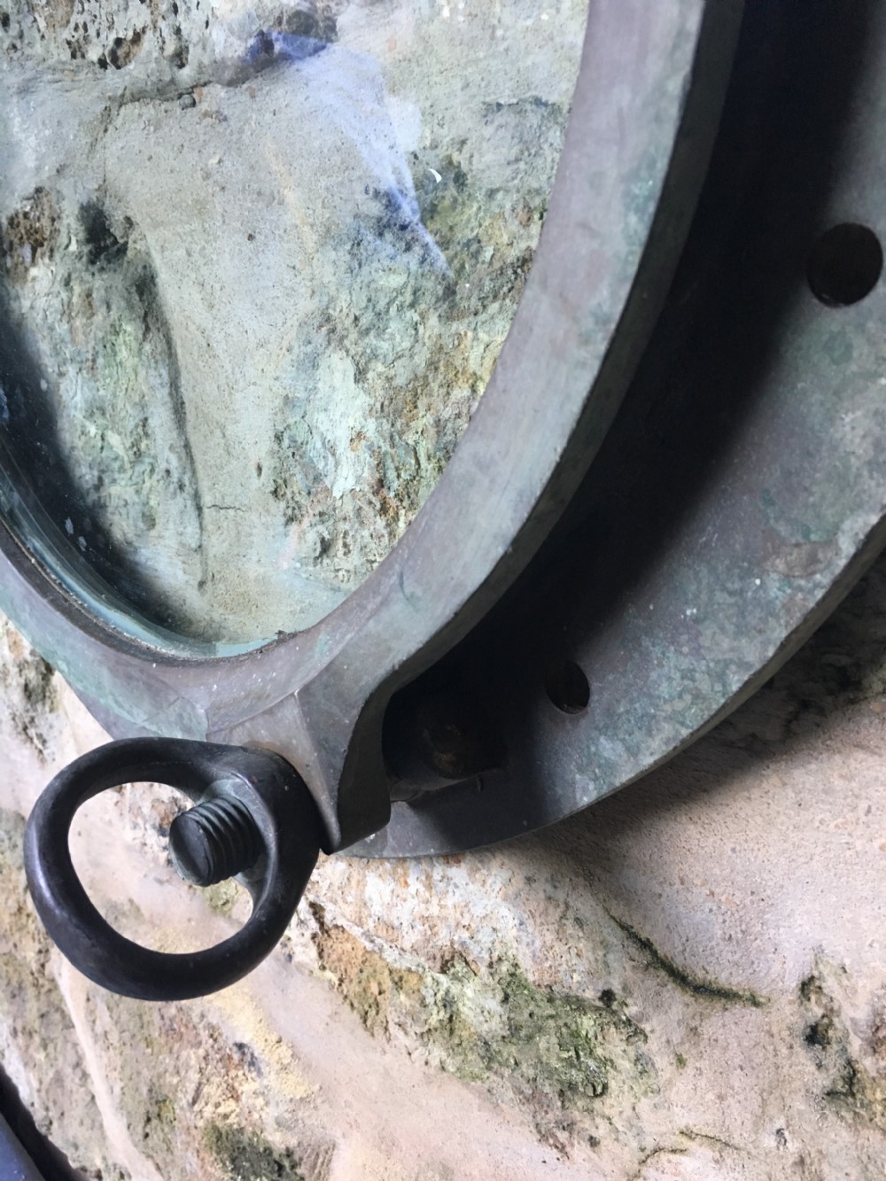 A heavy antique bronze circular ship porthole featuring visible hinge mounts, dog-bolt fasteners, a clear glass pane, and natural green patina. View XI