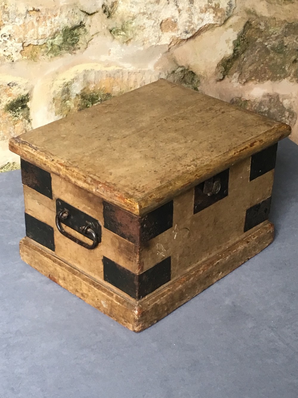 A small Victorian wooden trunk featuring an ochre painted finish, dark iron corner brackets, side handles, and a hinged lid.