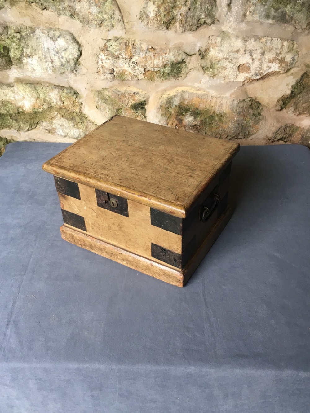 A small Victorian wooden trunk featuring an ochre painted finish, dark iron corner brackets, side handles, and a hinged lid. View VI