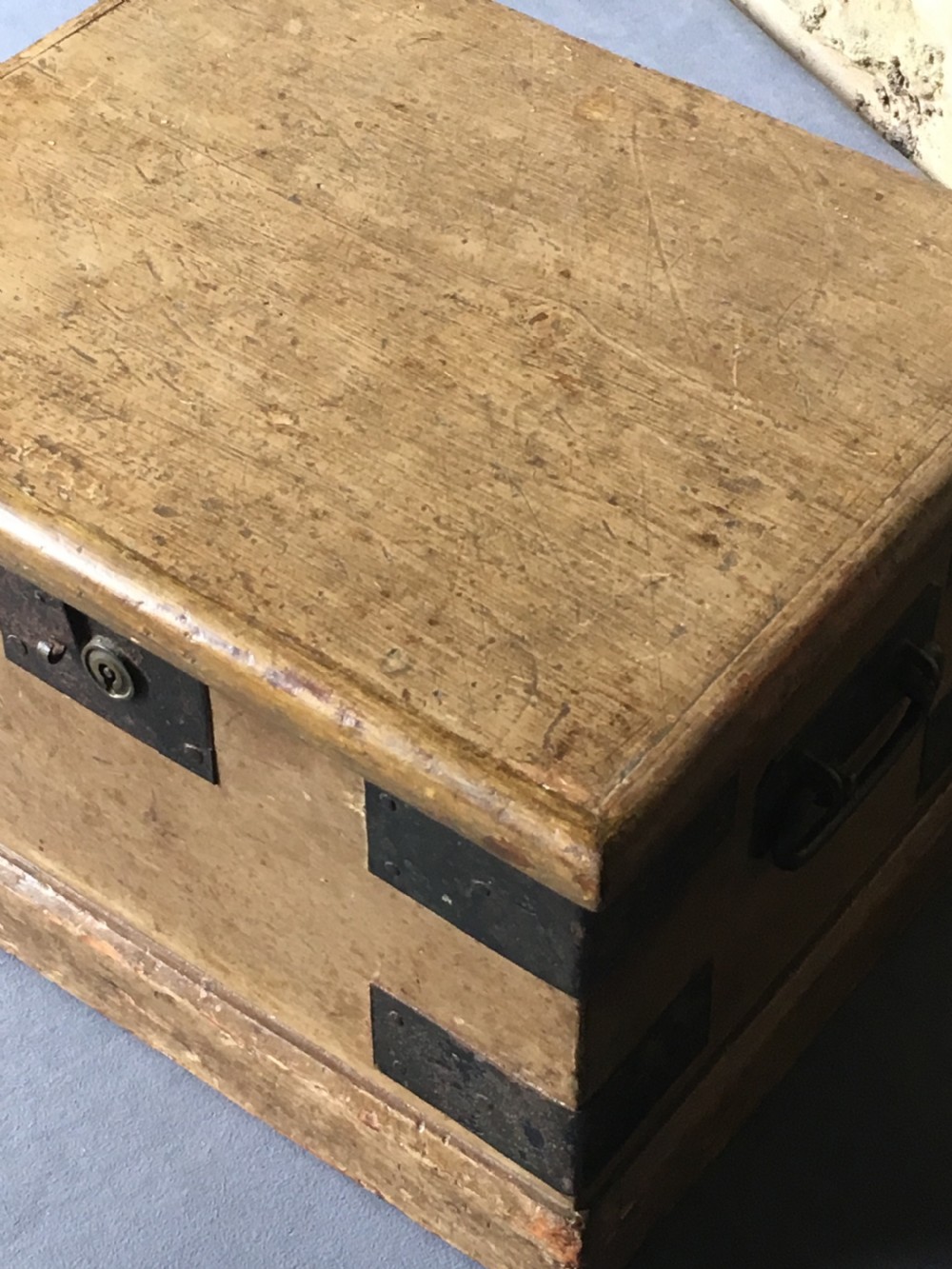 A small Victorian wooden trunk featuring an ochre painted finish, dark iron corner brackets, side handles, and a hinged lid. View X