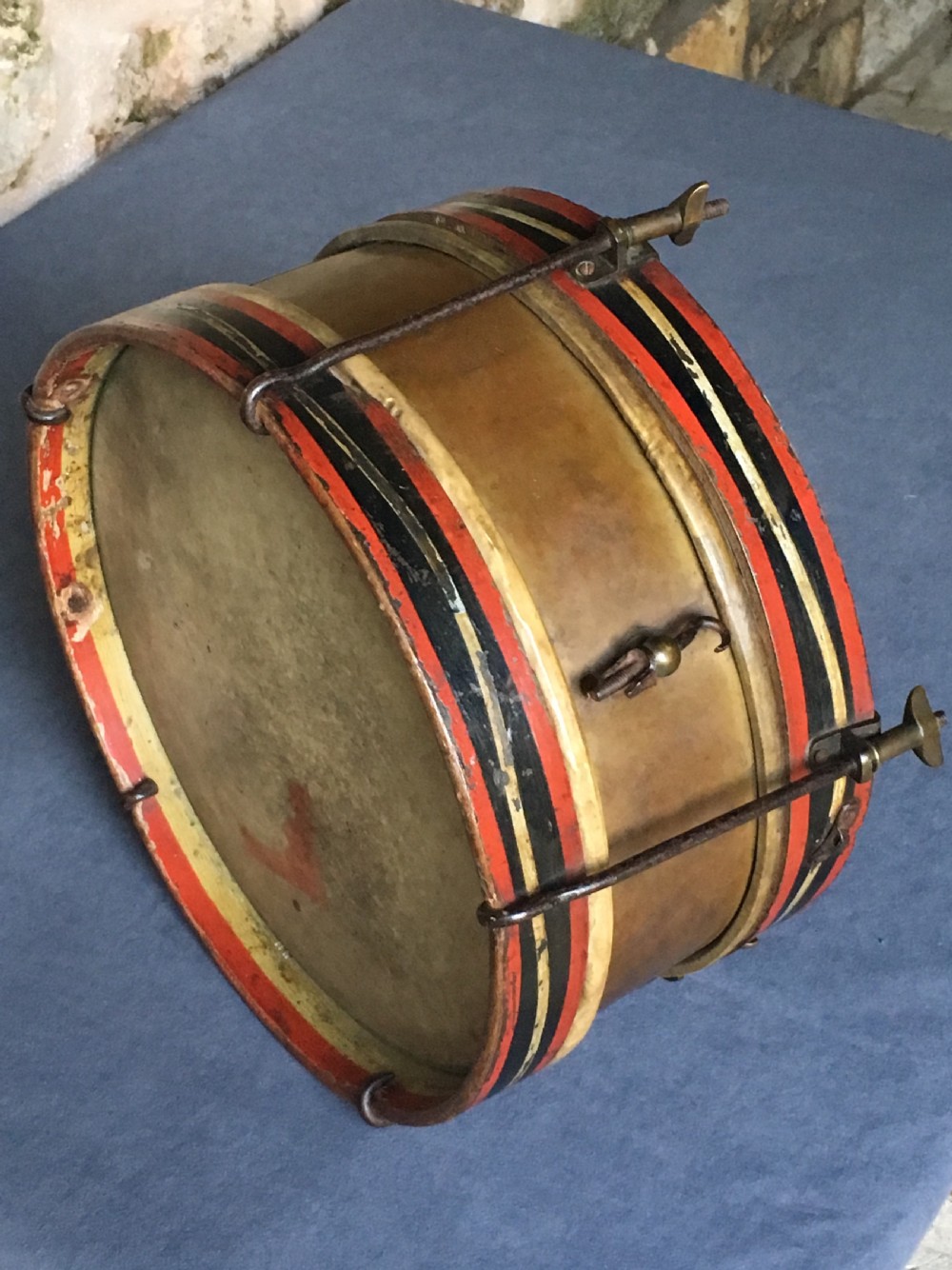 An early twentieth-century drum featuring a brass body, skin drumhead, tension rods, and painted wooden hoops with red, black, and cream stripes.