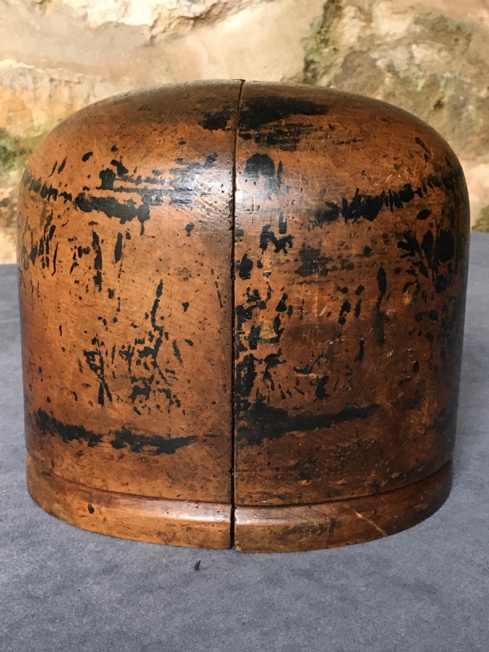A two-piece carved wooden milliners hat block featuring a rounded dome top and a weathered brown and black painted finish.