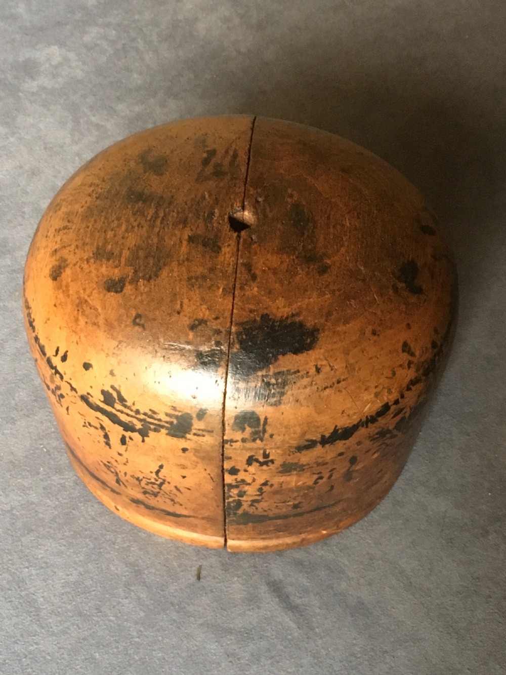 A two-piece carved wooden milliners hat block featuring a rounded dome top and a weathered brown and black painted finish. View XII