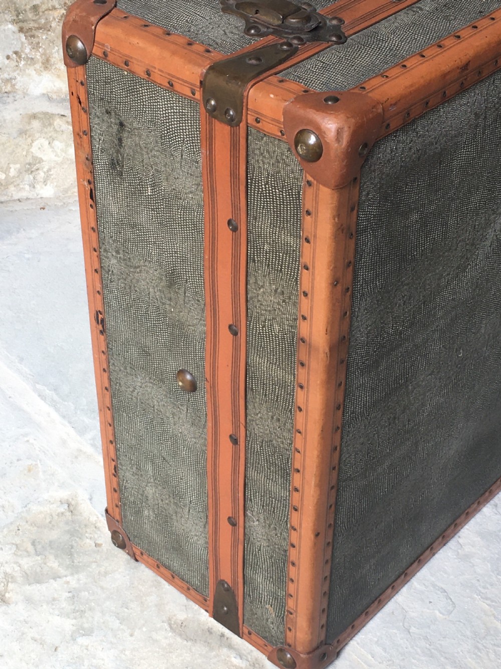 An antique French hard-sided luggage suitcase featuring grey canvas, tan leather trim, brass hardware, and a leather carrying handle. View IV