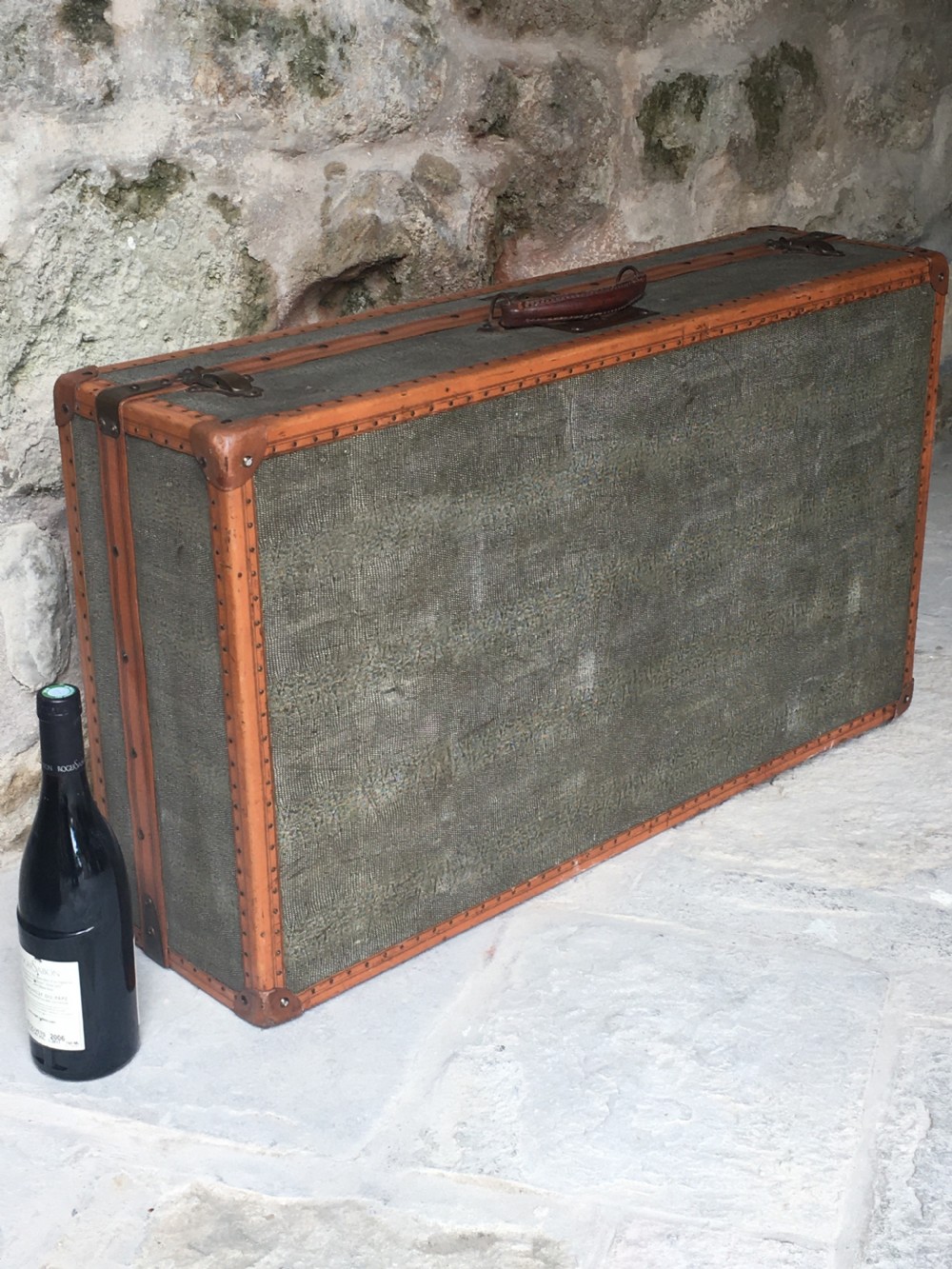 An antique French hard-sided luggage suitcase featuring grey canvas, tan leather trim, brass hardware, and a leather carrying handle. View VIII