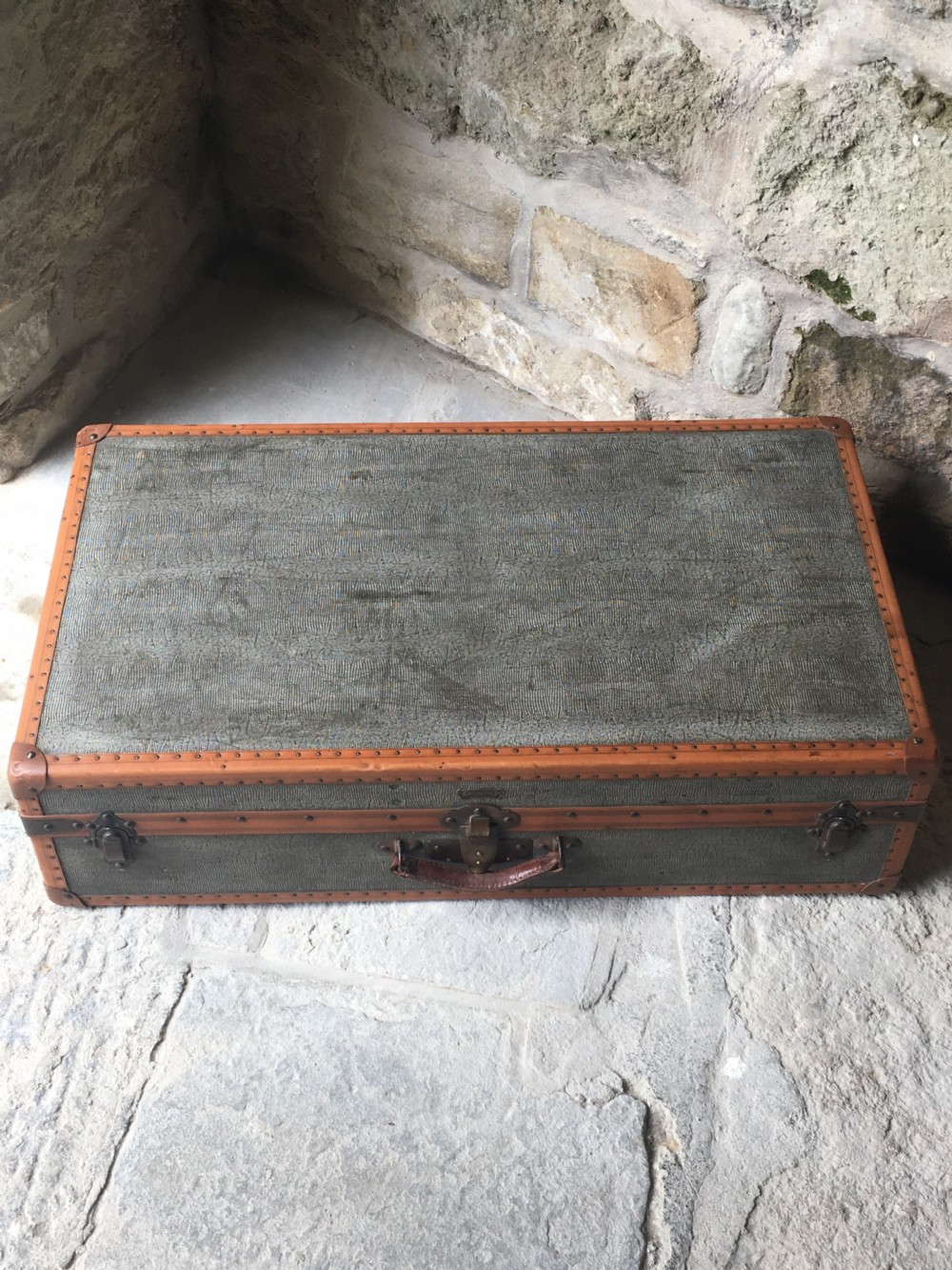 An antique French hard-sided luggage suitcase featuring grey canvas, tan leather trim, brass hardware, and a leather carrying handle. View XI