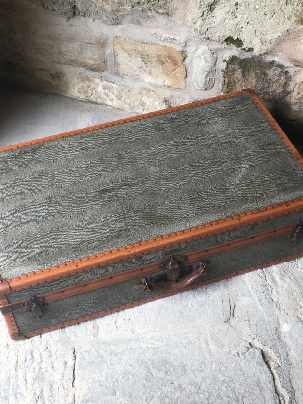 An antique French hard-sided luggage suitcase featuring grey canvas, tan leather trim, brass hardware, and a leather carrying handle. View XII