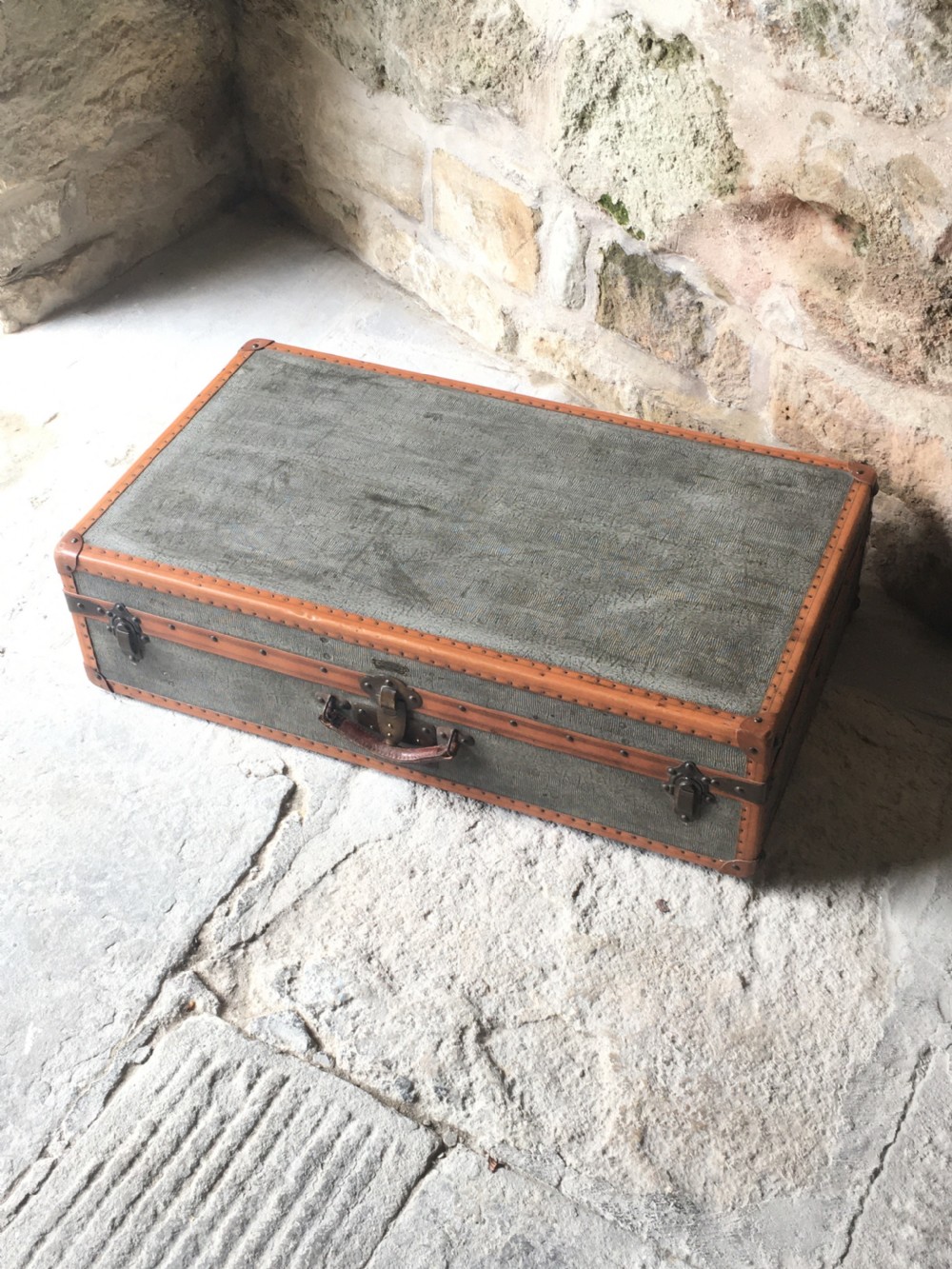 An antique French hard-sided luggage suitcase featuring grey canvas, tan leather trim, brass hardware, and a leather carrying handle. View XIII