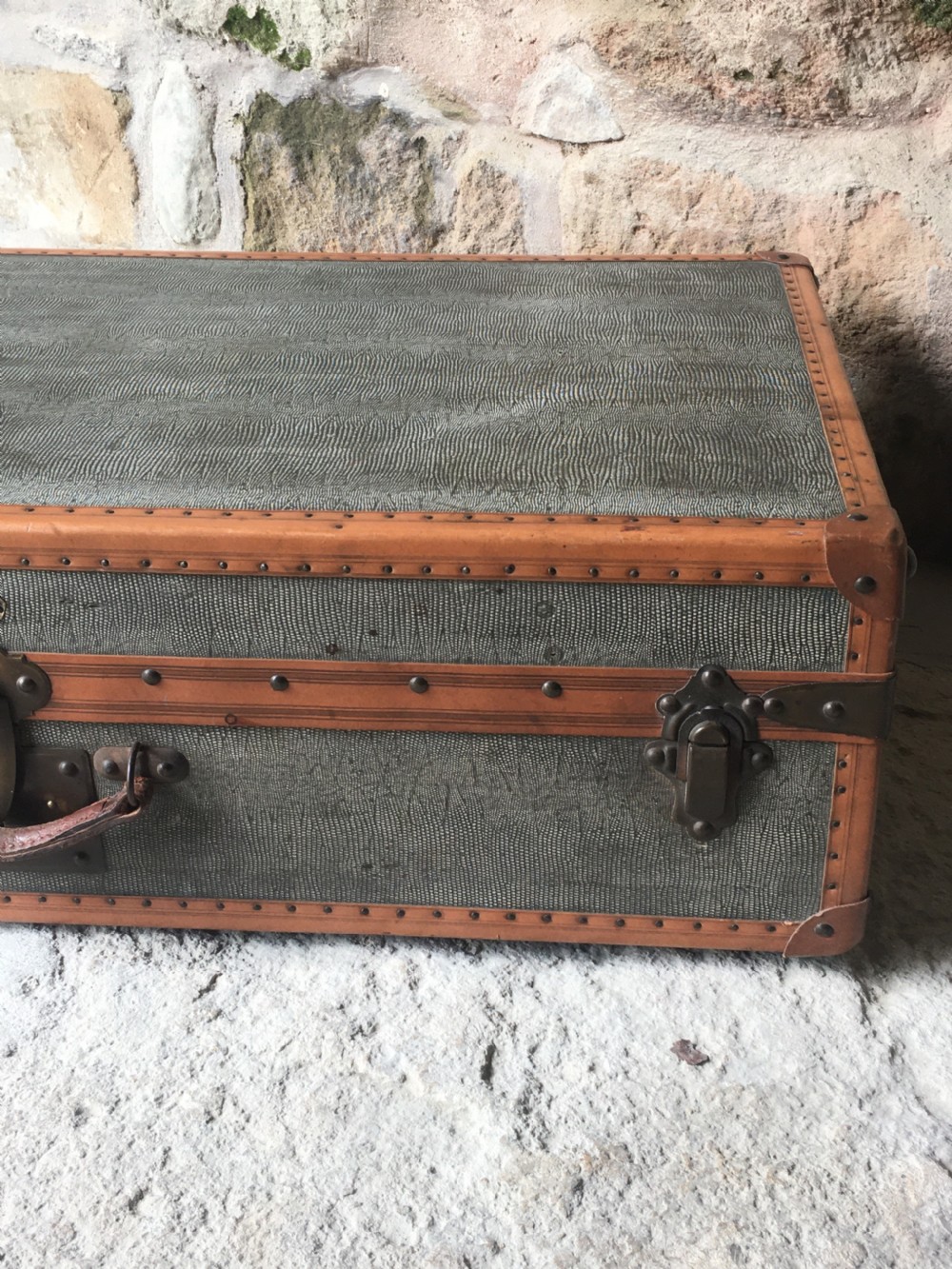 An antique French hard-sided luggage suitcase featuring grey canvas, tan leather trim, brass hardware, and a leather carrying handle. View XIV