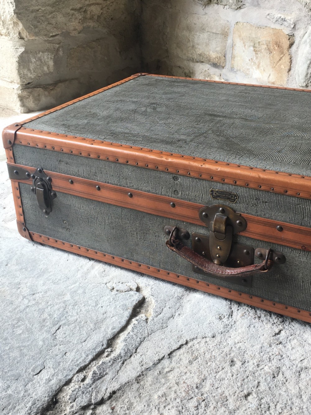 An antique French hard-sided luggage suitcase featuring grey canvas, tan leather trim, brass hardware, and a leather carrying handle. View XV