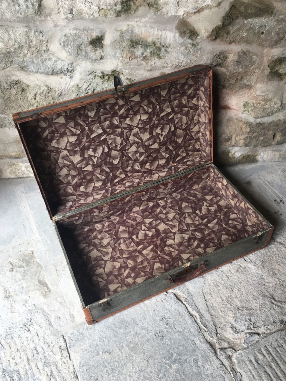 An antique French hard-sided luggage suitcase featuring grey canvas, tan leather trim, brass hardware, and a leather carrying handle. View XVI