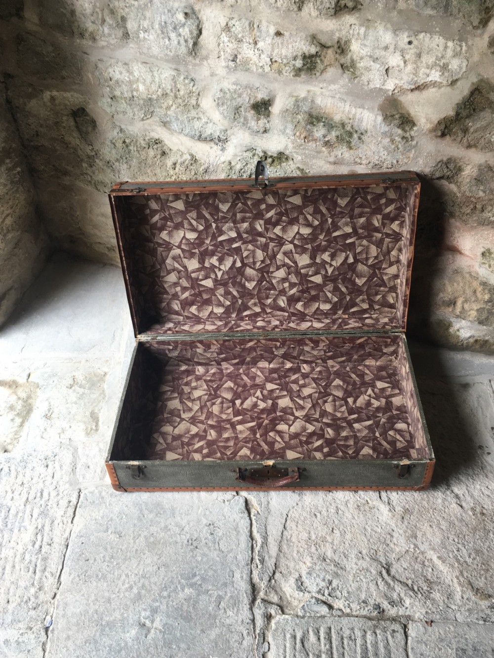 An antique French hard-sided luggage suitcase featuring grey canvas, tan leather trim, brass hardware, and a leather carrying handle. View XVII