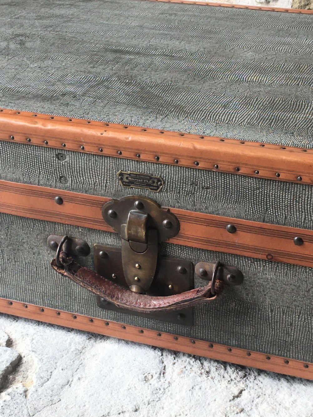 An antique French hard-sided luggage suitcase featuring grey canvas, tan leather trim, brass hardware, and a leather carrying handle. View XVIII