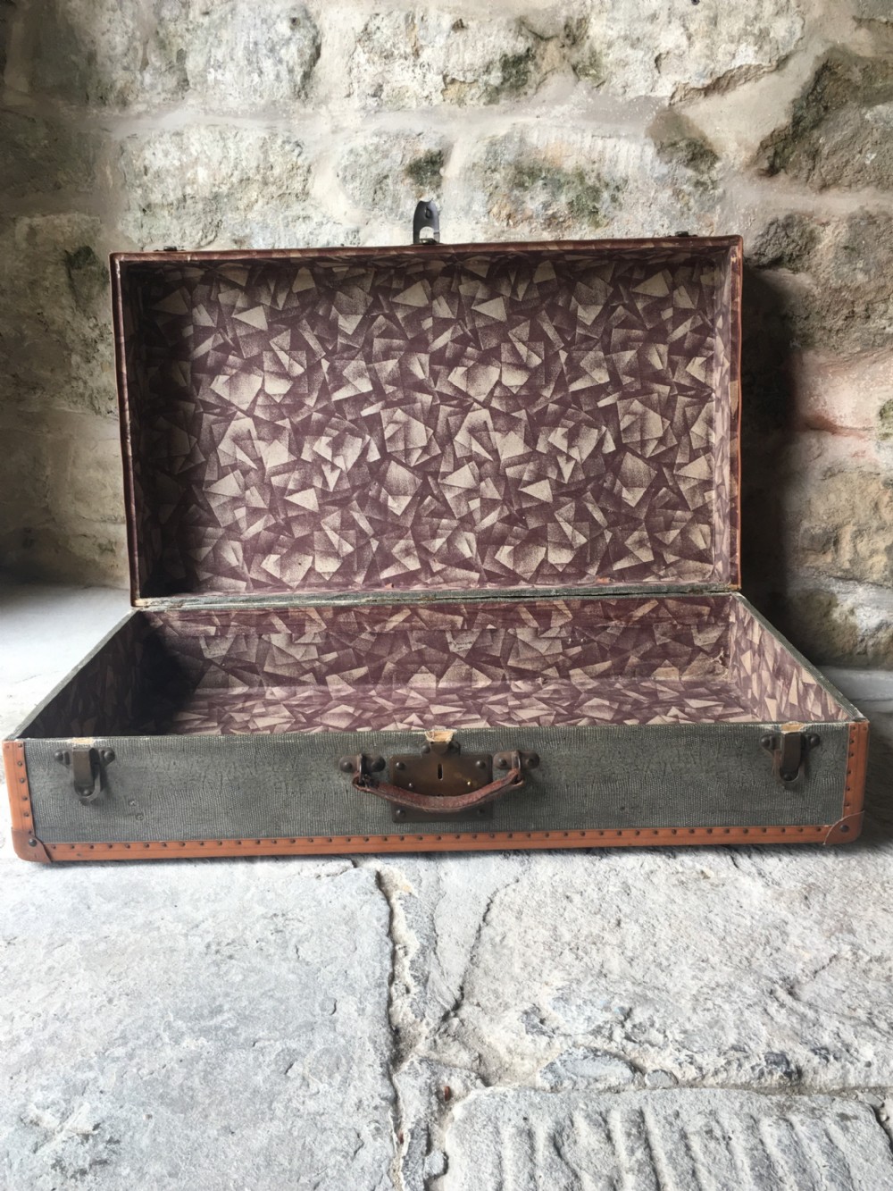 An antique French hard-sided luggage suitcase featuring grey canvas, tan leather trim, brass hardware, and a leather carrying handle. View XIX