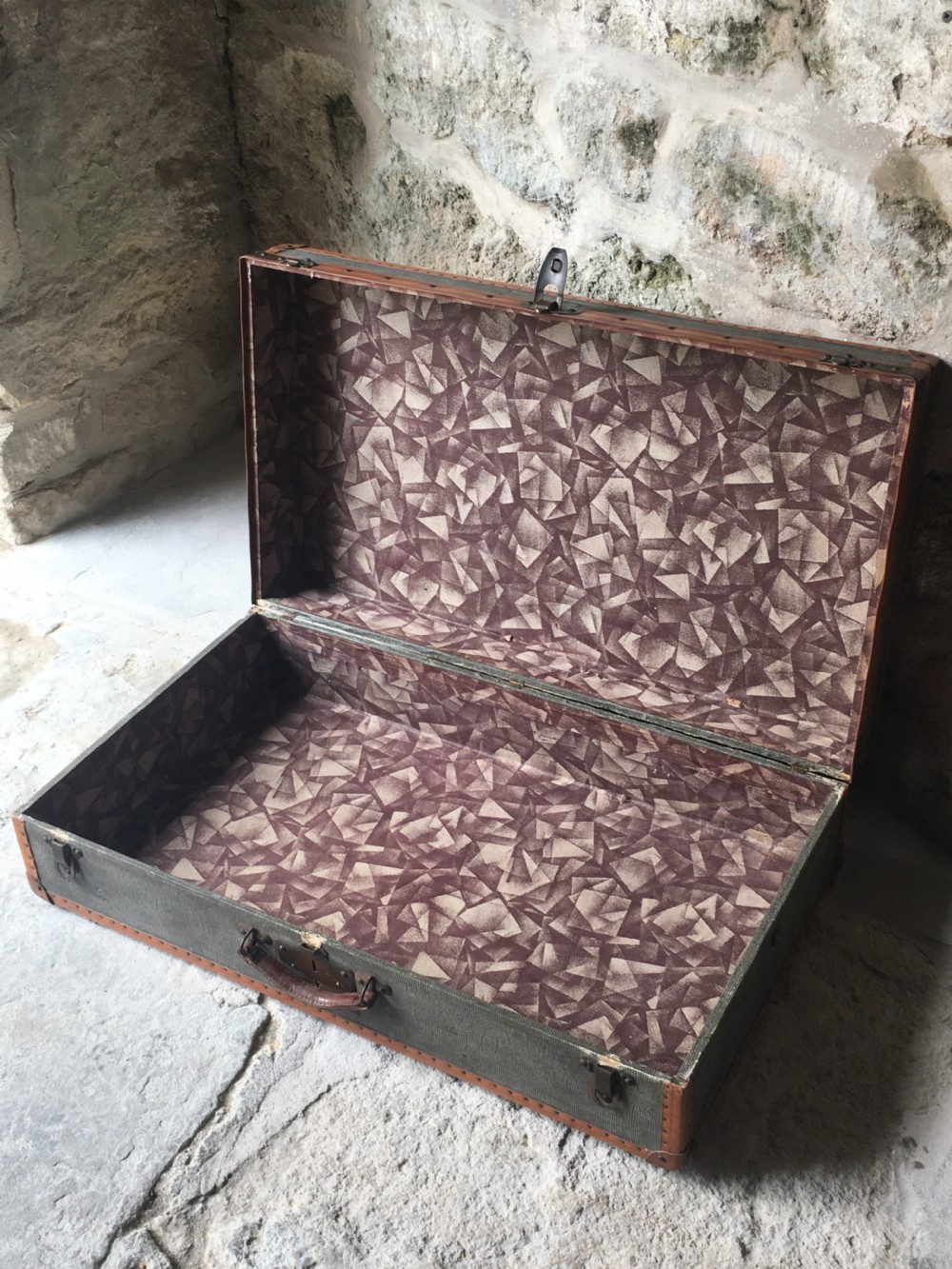 An antique French hard-sided luggage suitcase featuring grey canvas, tan leather trim, brass hardware, and a leather carrying handle. View XX