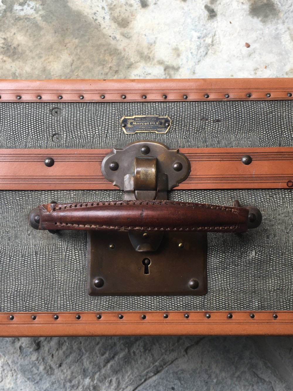 An antique French hard-sided luggage suitcase featuring grey canvas, tan leather trim, brass hardware, and a leather carrying handle. View XXI