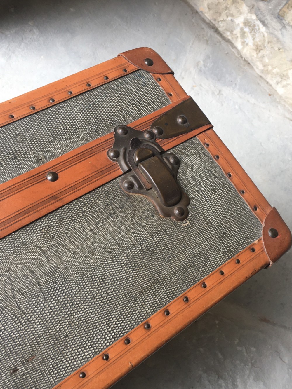 An antique French hard-sided luggage suitcase featuring grey canvas, tan leather trim, brass hardware, and a leather carrying handle. View XXIII