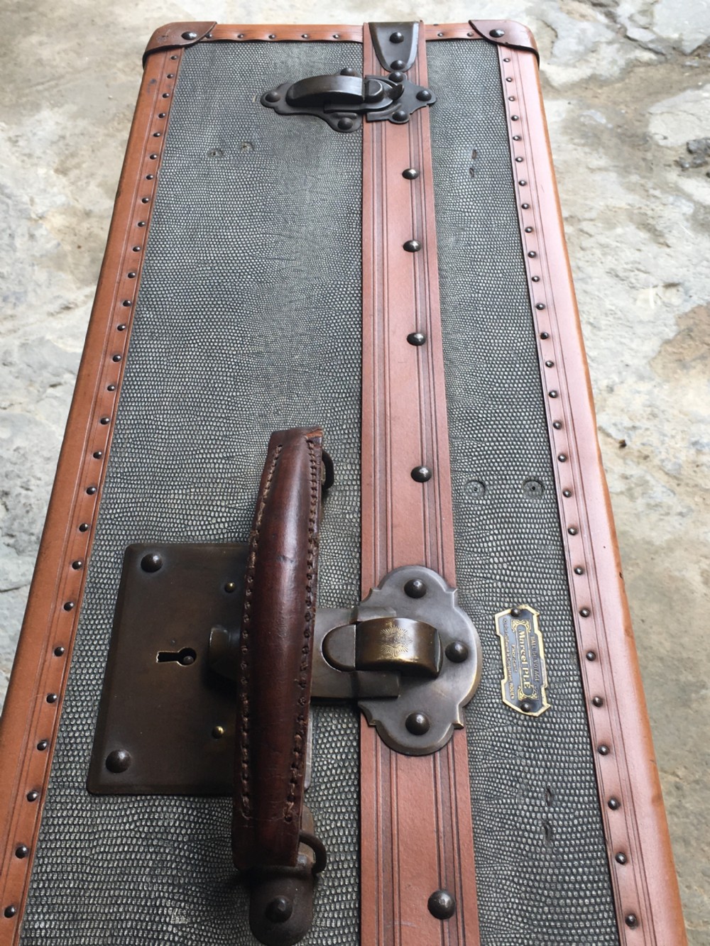 An antique French hard-sided luggage suitcase featuring grey canvas, tan leather trim, brass hardware, and a leather carrying handle. View XXV