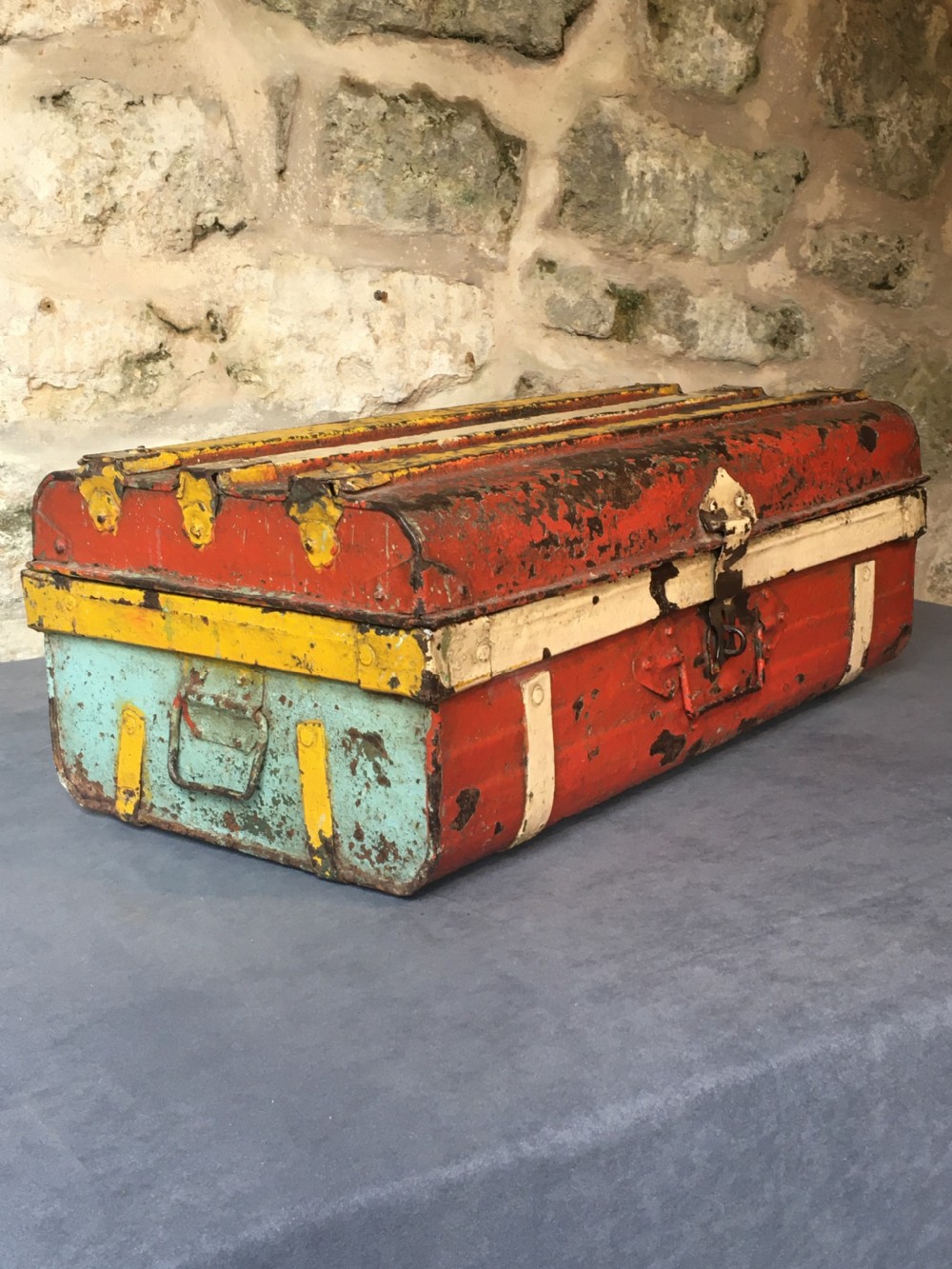 A rectangular early twentieth-century painted sheet metal trunk with ribbed details, metal latches, and distressed red, yellow, cream, and turquoise paintwork.
