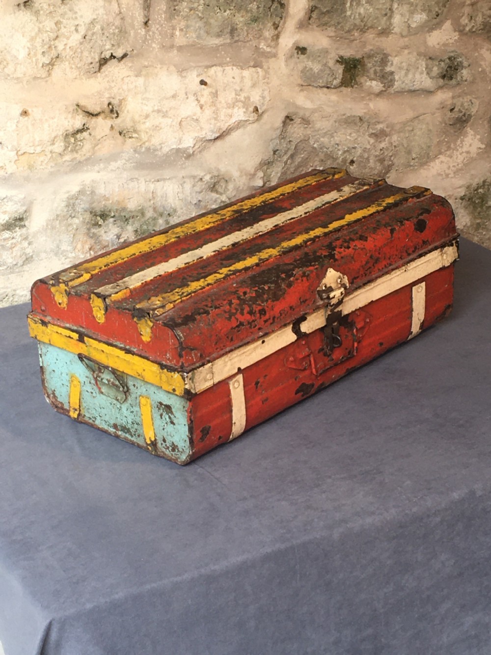 A rectangular early twentieth-century painted sheet metal trunk with ribbed details, metal latches, and distressed red, yellow, cream, and turquoise paintwork. View II