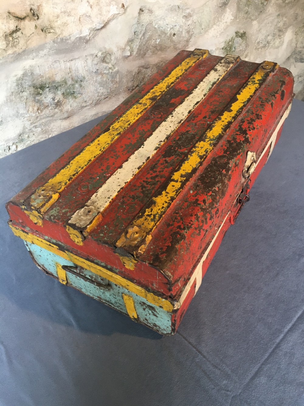 A rectangular early twentieth-century painted sheet metal trunk with ribbed details, metal latches, and distressed red, yellow, cream, and turquoise paintwork. View III