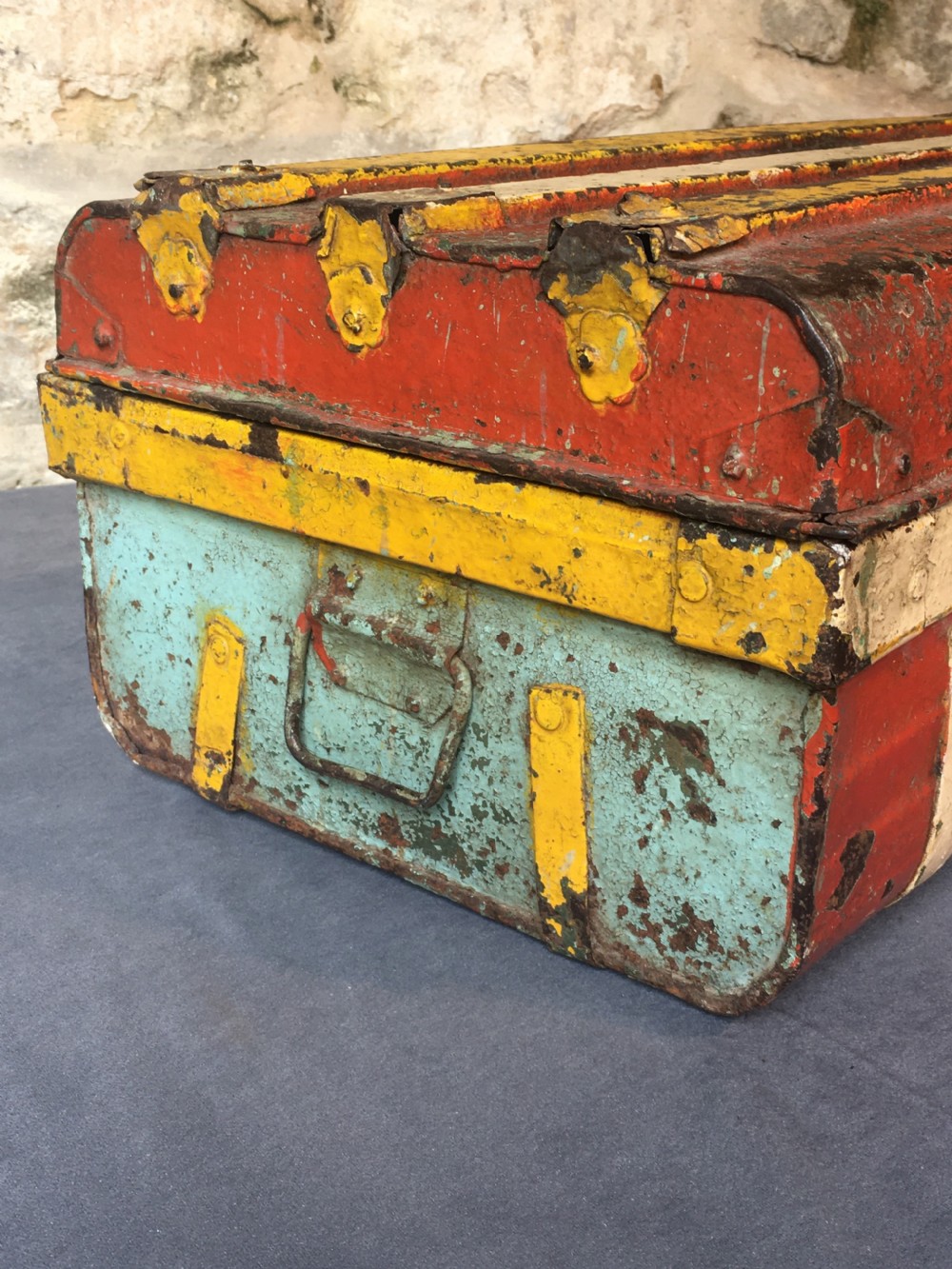 A rectangular early twentieth-century painted sheet metal trunk with ribbed details, metal latches, and distressed red, yellow, cream, and turquoise paintwork. View IV