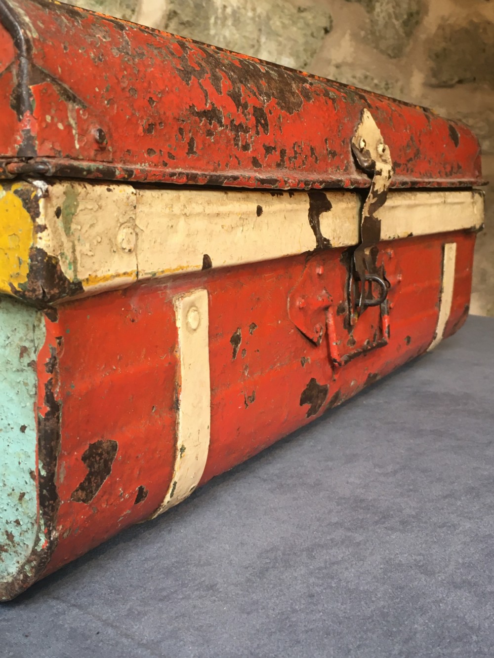 A rectangular early twentieth-century painted sheet metal trunk with ribbed details, metal latches, and distressed red, yellow, cream, and turquoise paintwork. View V
