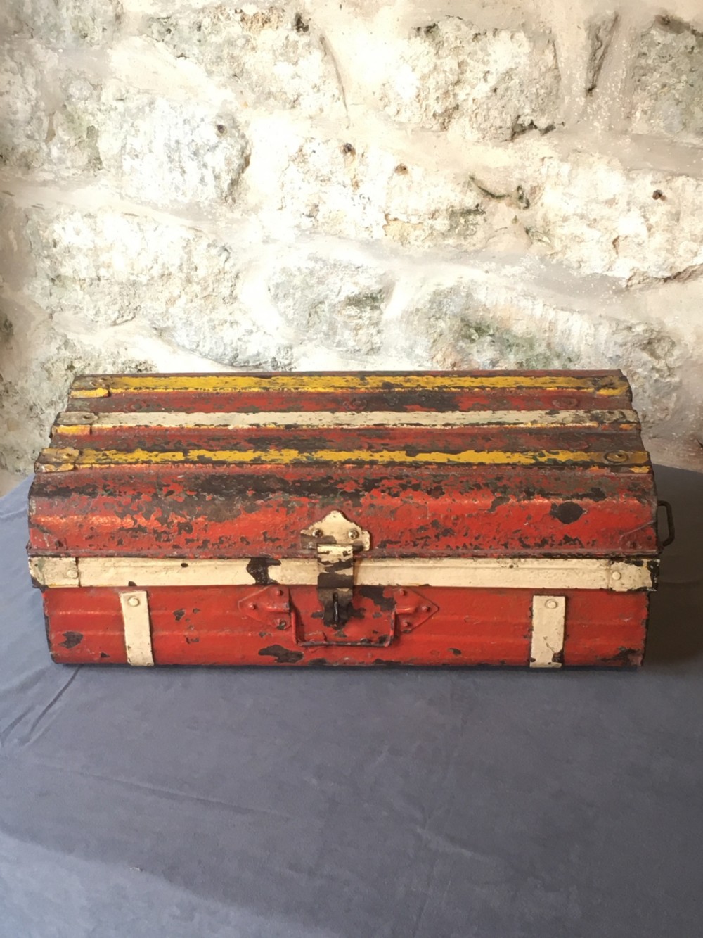 A rectangular early twentieth-century painted sheet metal trunk with ribbed details, metal latches, and distressed red, yellow, cream, and turquoise paintwork. View VI