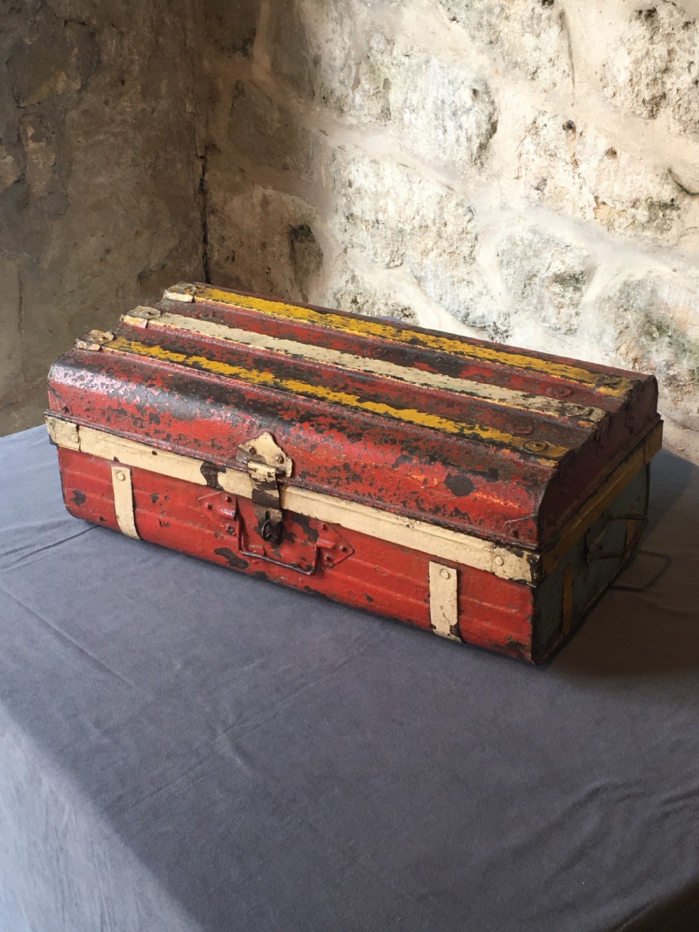 A rectangular early twentieth-century painted sheet metal trunk with ribbed details, metal latches, and distressed red, yellow, cream, and turquoise paintwork. View VII
