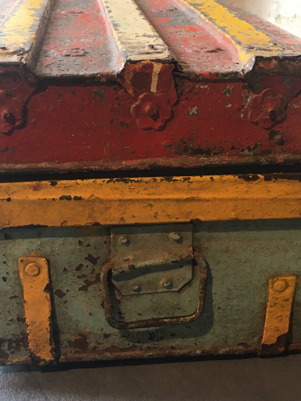 A rectangular early twentieth-century painted sheet metal trunk with ribbed details, metal latches, and distressed red, yellow, cream, and turquoise paintwork. View VIII