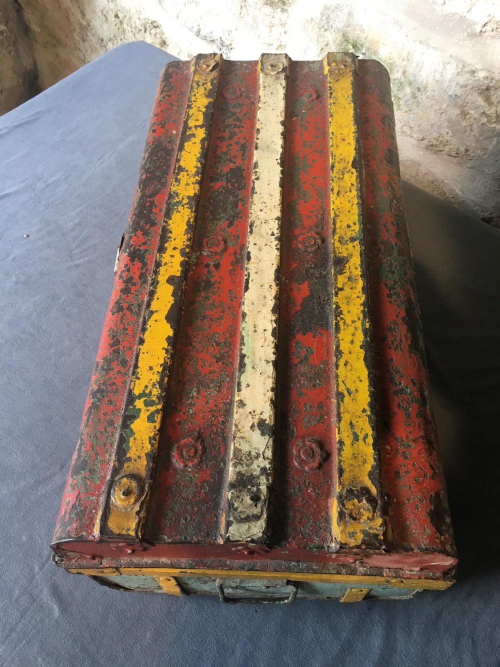 A rectangular early twentieth-century painted sheet metal trunk with ribbed details, metal latches, and distressed red, yellow, cream, and turquoise paintwork. View IX