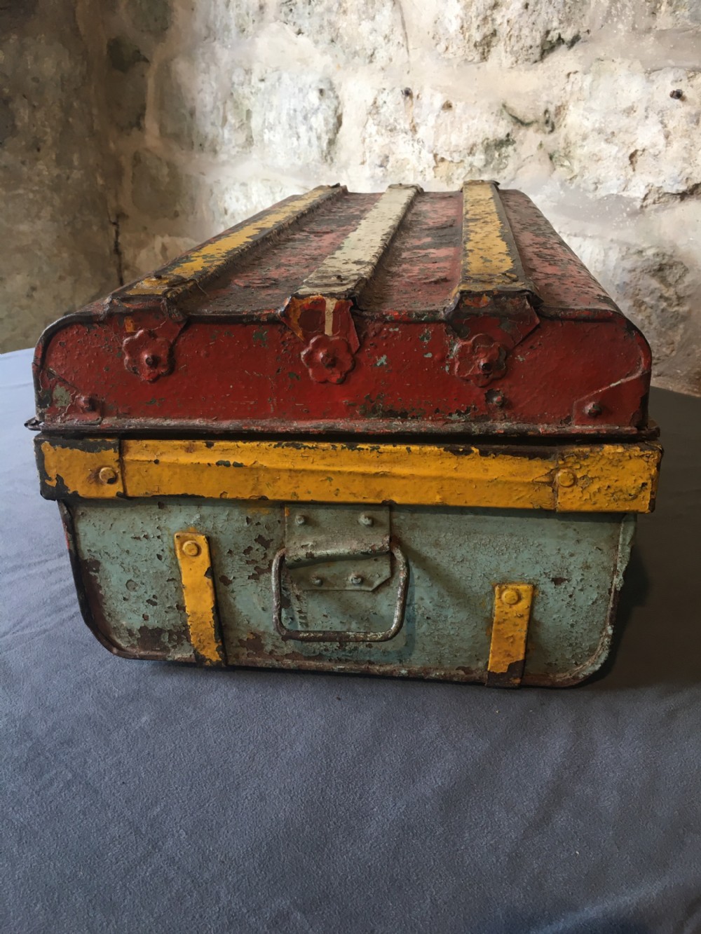 A rectangular early twentieth-century painted sheet metal trunk with ribbed details, metal latches, and distressed red, yellow, cream, and turquoise paintwork. View X