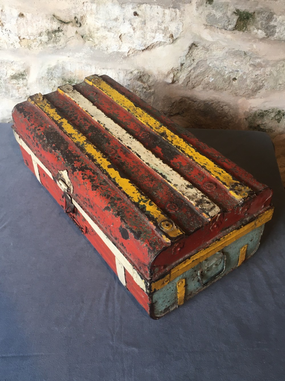 A rectangular early twentieth-century painted sheet metal trunk with ribbed details, metal latches, and distressed red, yellow, cream, and turquoise paintwork. View XI