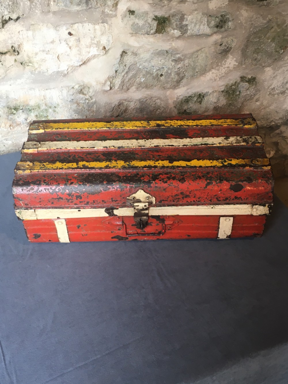 A rectangular early twentieth-century painted sheet metal trunk with ribbed details, metal latches, and distressed red, yellow, cream, and turquoise paintwork. View XII