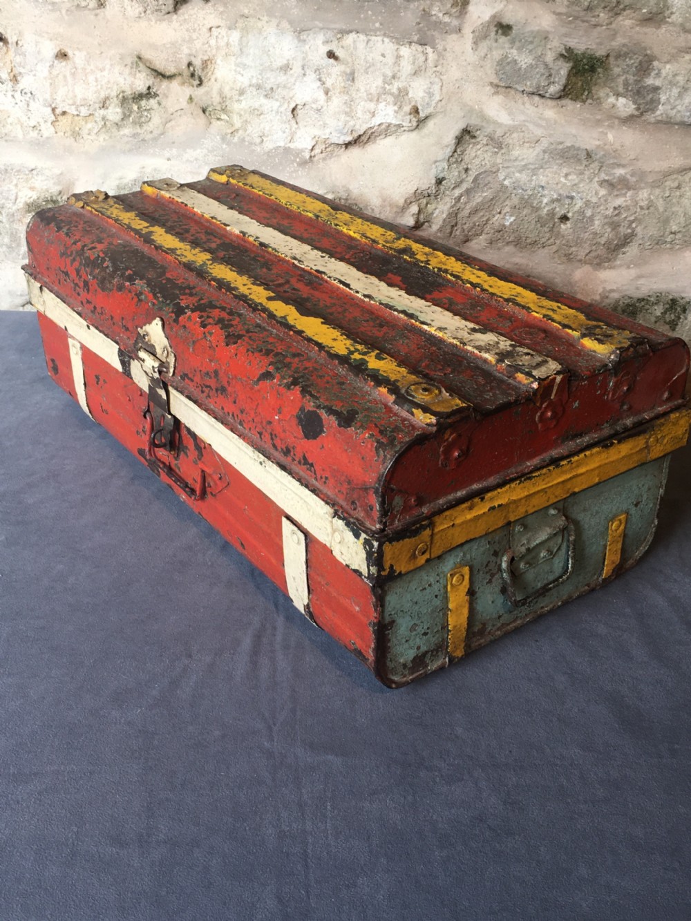 A rectangular early twentieth-century painted sheet metal trunk with ribbed details, metal latches, and distressed red, yellow, cream, and turquoise paintwork. View XIII