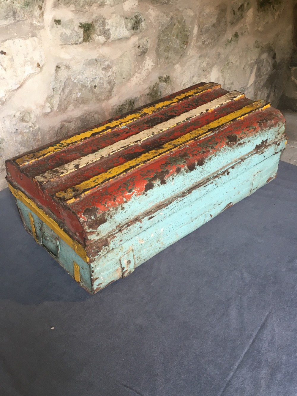 A rectangular early twentieth-century painted sheet metal trunk with ribbed details, metal latches, and distressed red, yellow, cream, and turquoise paintwork. View XV