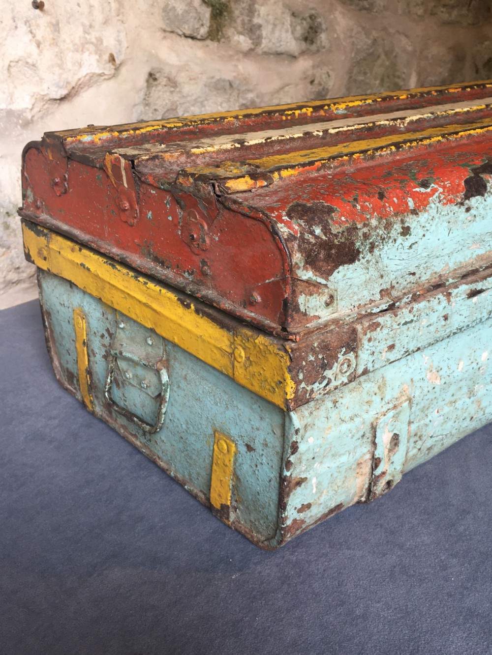 A rectangular early twentieth-century painted sheet metal trunk with ribbed details, metal latches, and distressed red, yellow, cream, and turquoise paintwork. View XVI