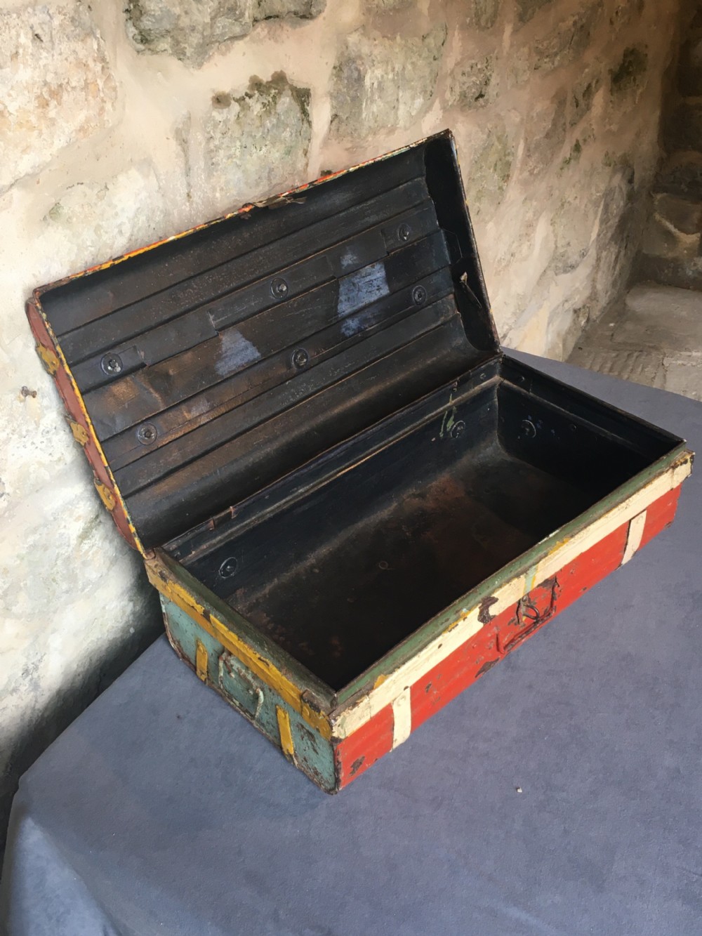 A rectangular early twentieth-century painted sheet metal trunk with ribbed details, metal latches, and distressed red, yellow, cream, and turquoise paintwork. View XVII