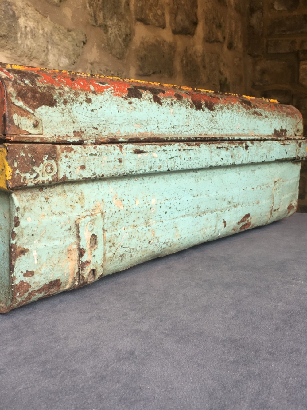 A rectangular early twentieth-century painted sheet metal trunk with ribbed details, metal latches, and distressed red, yellow, cream, and turquoise paintwork. View XVIII