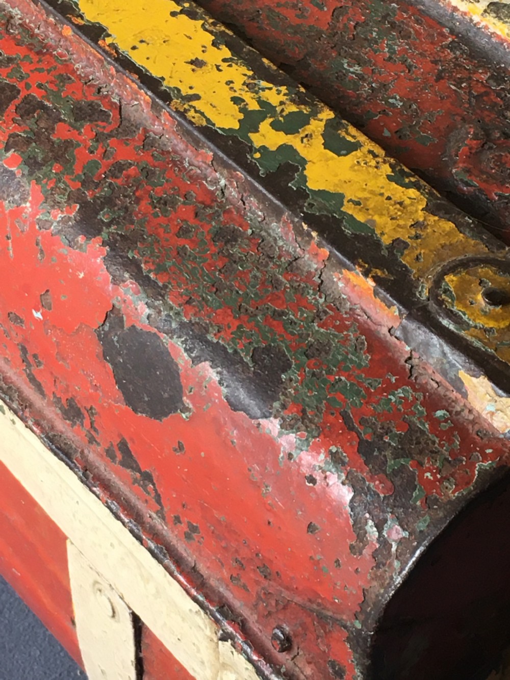 A rectangular early twentieth-century painted sheet metal trunk with ribbed details, metal latches, and distressed red, yellow, cream, and turquoise paintwork. View XX