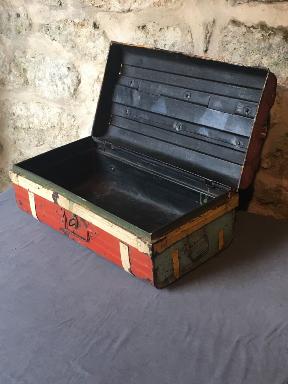 A rectangular early twentieth-century painted sheet metal trunk with ribbed details, metal latches, and distressed red, yellow, cream, and turquoise paintwork. View XXI
