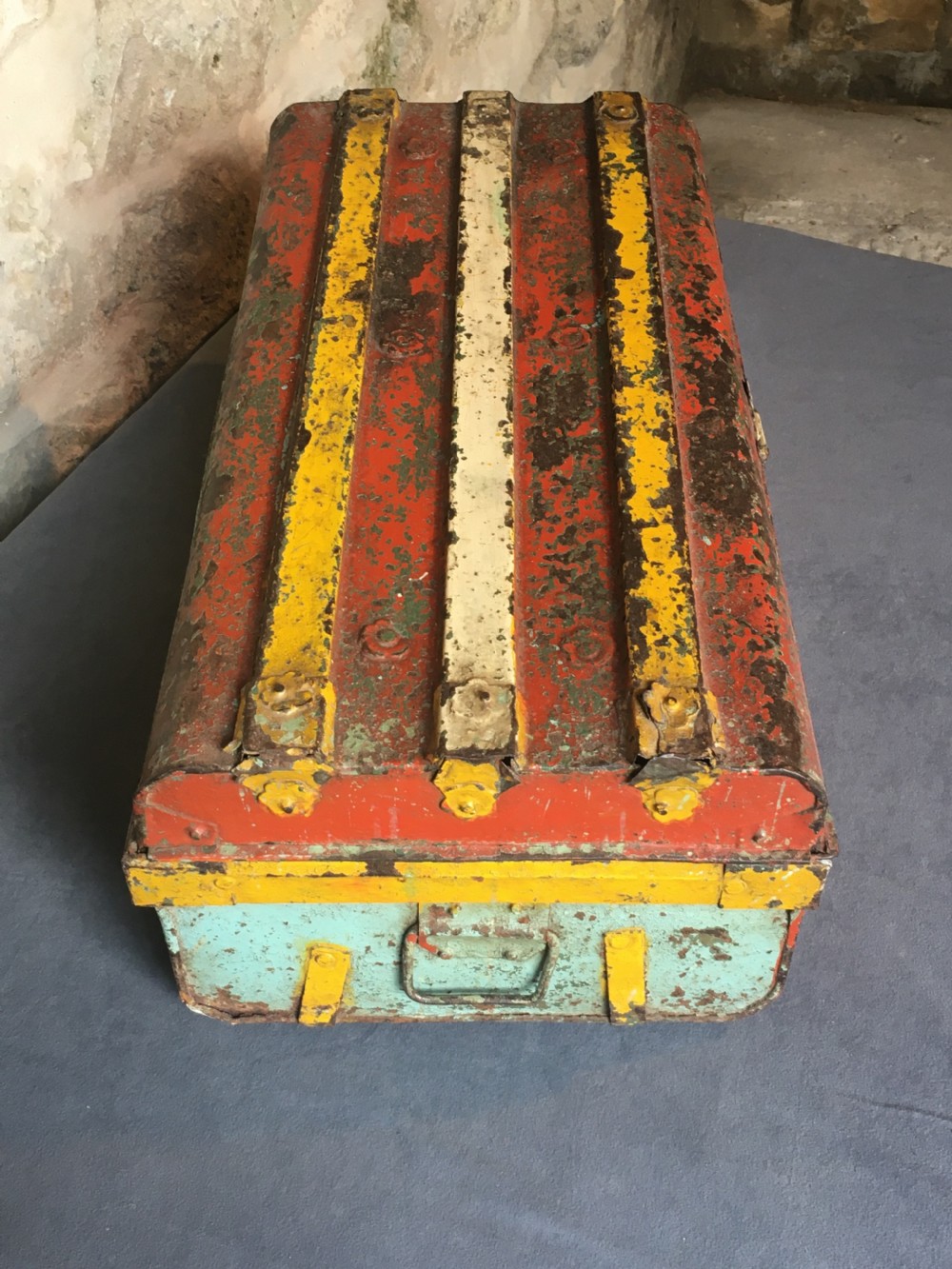 A rectangular early twentieth-century painted sheet metal trunk with ribbed details, metal latches, and distressed red, yellow, cream, and turquoise paintwork. View XXIV