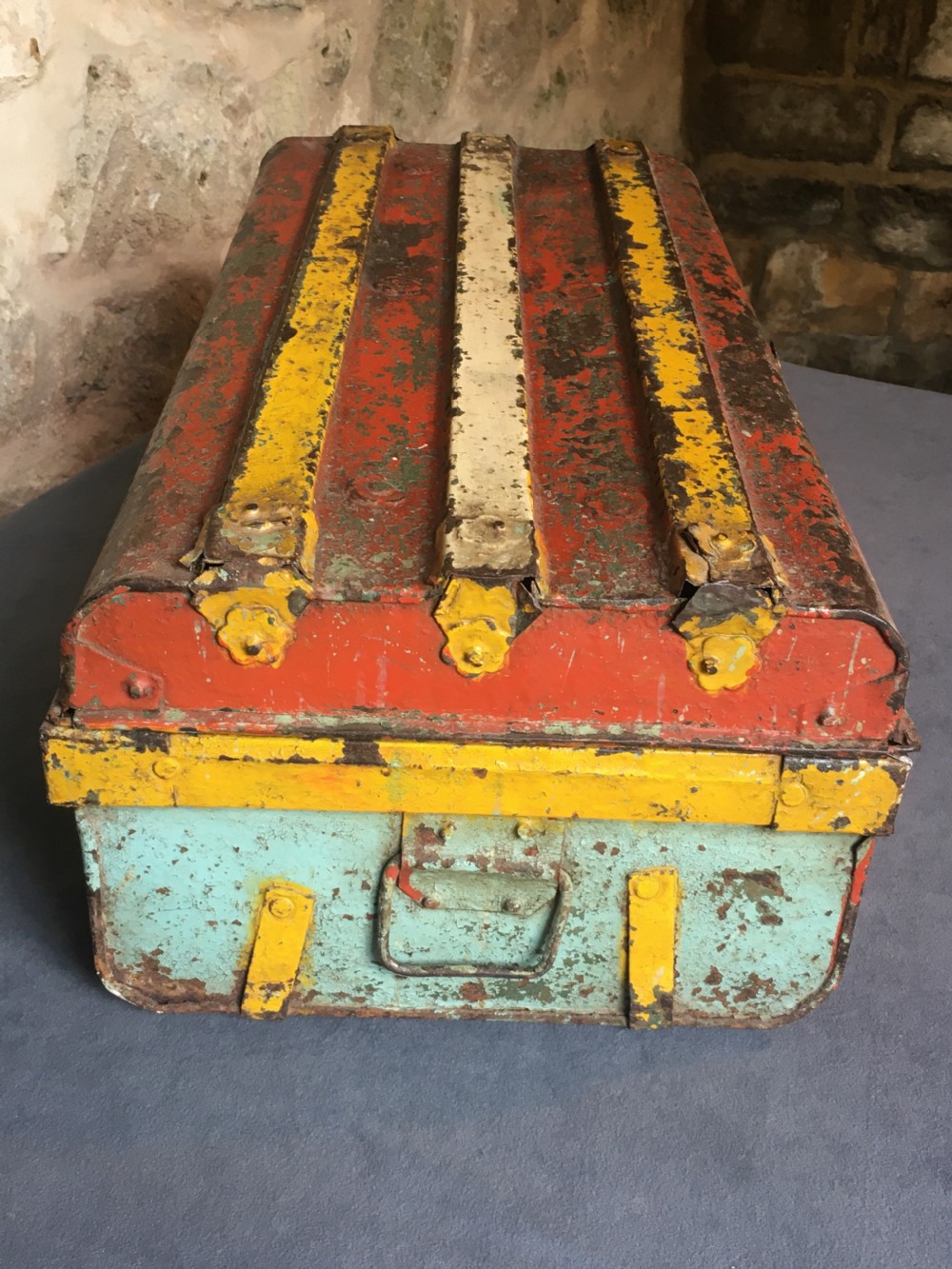 A rectangular early twentieth-century painted sheet metal trunk with ribbed details, metal latches, and distressed red, yellow, cream, and turquoise paintwork. View XXV