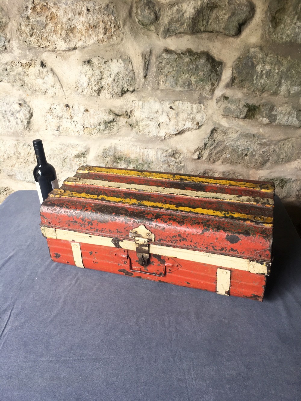 A rectangular early twentieth-century painted sheet metal trunk with ribbed details, metal latches, and distressed red, yellow, cream, and turquoise paintwork. View XXVI