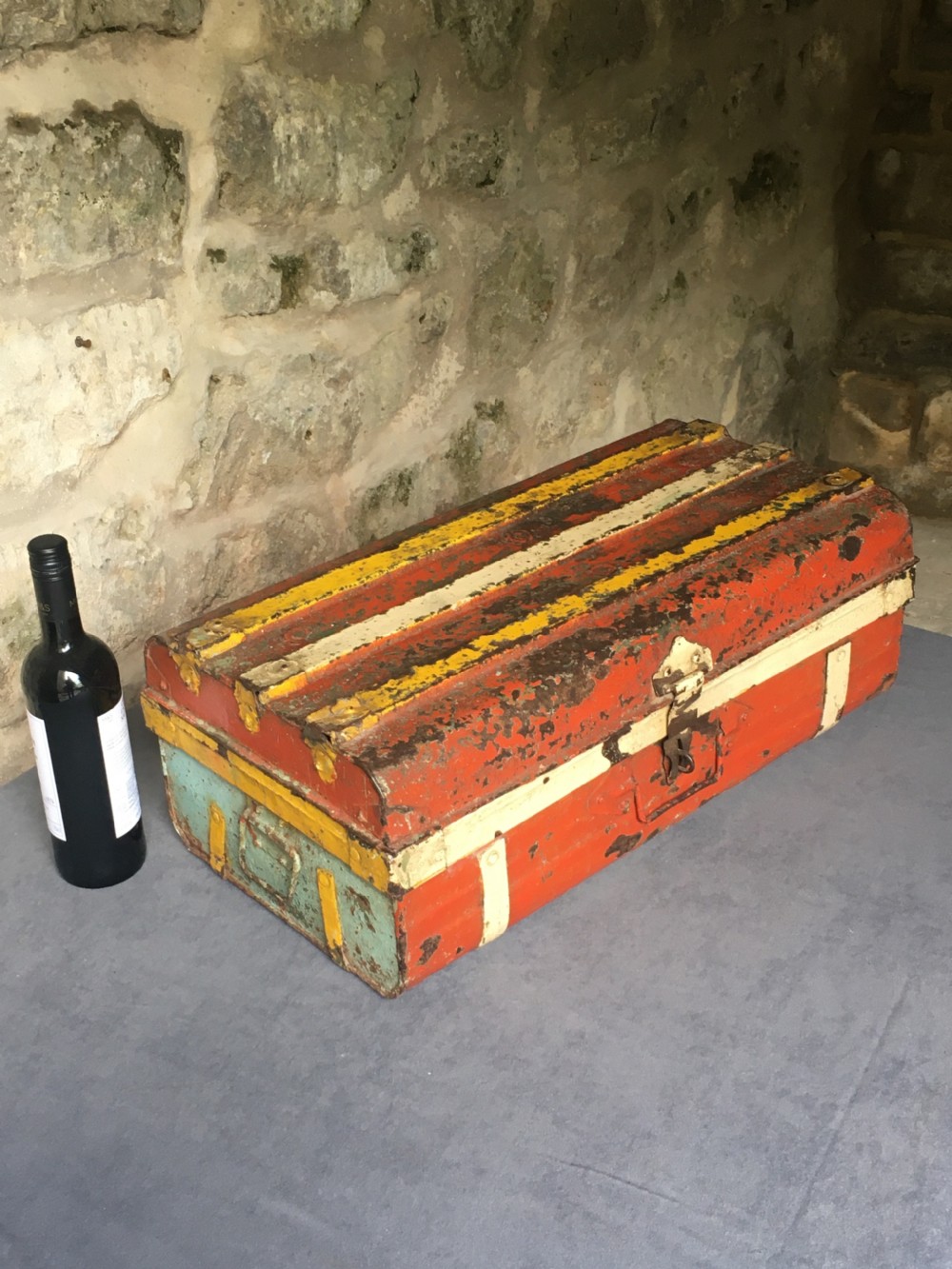 A rectangular early twentieth-century painted sheet metal trunk with ribbed details, metal latches, and distressed red, yellow, cream, and turquoise paintwork. View XXVII
