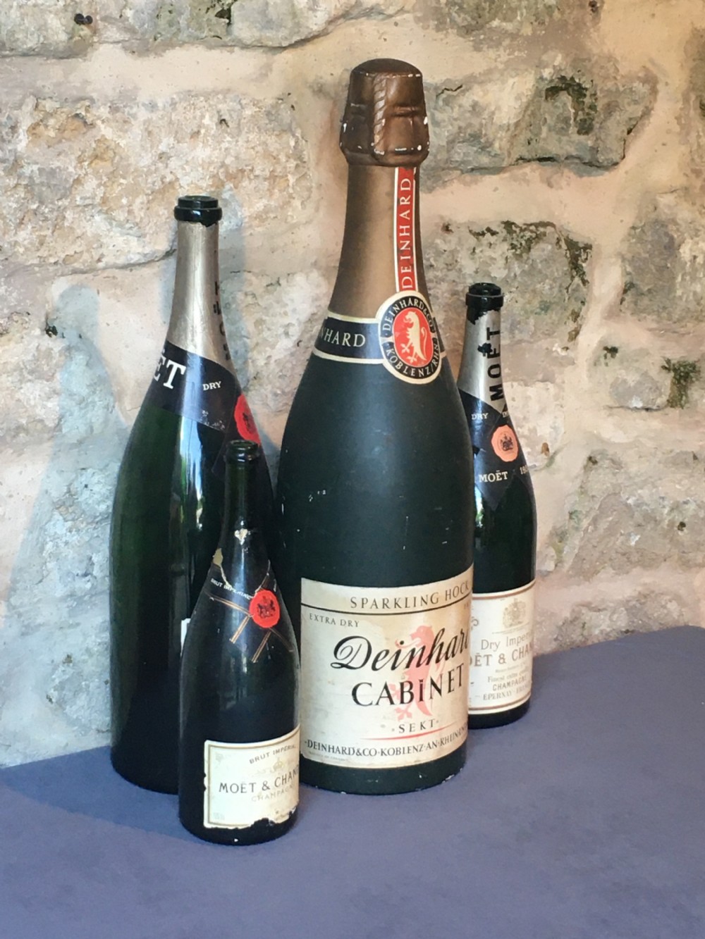 A group of four large vintage dark green glass advertising wine and champagne bottles featuring original paper labels.