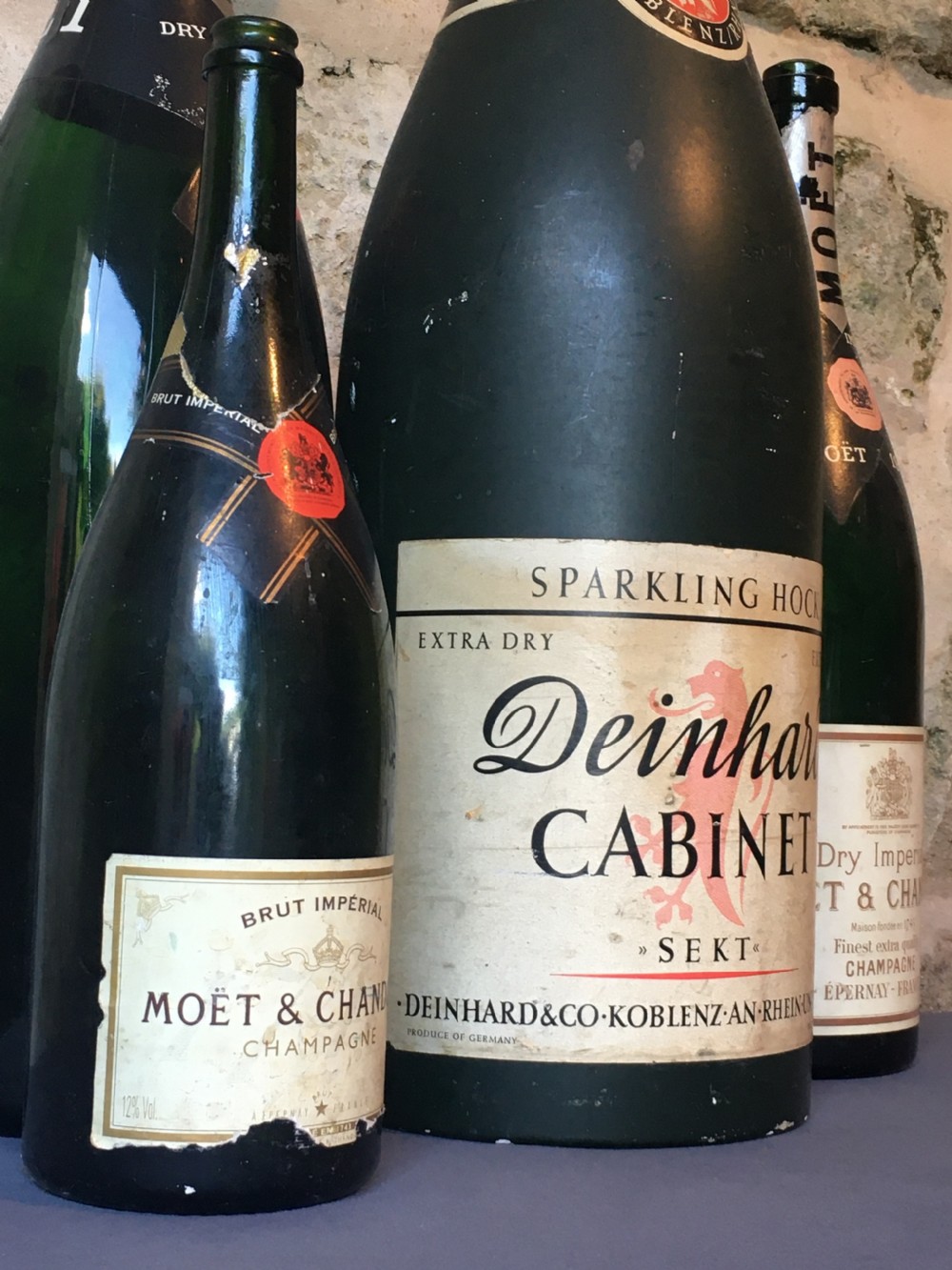 A group of four large vintage dark green glass advertising wine and champagne bottles featuring original paper labels. View IX